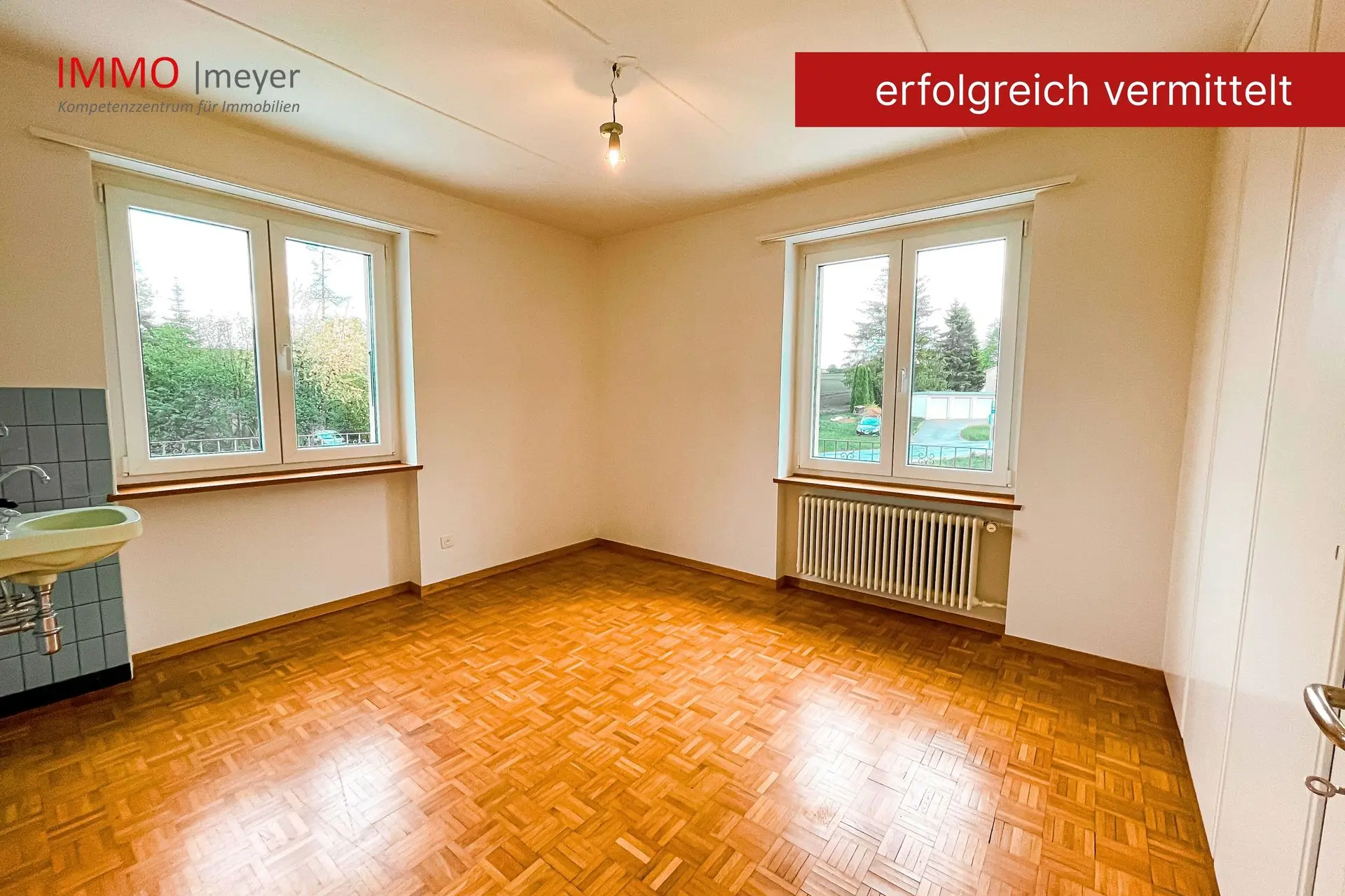 Wohnraum mit Parkettboden und zwei Fenstern
