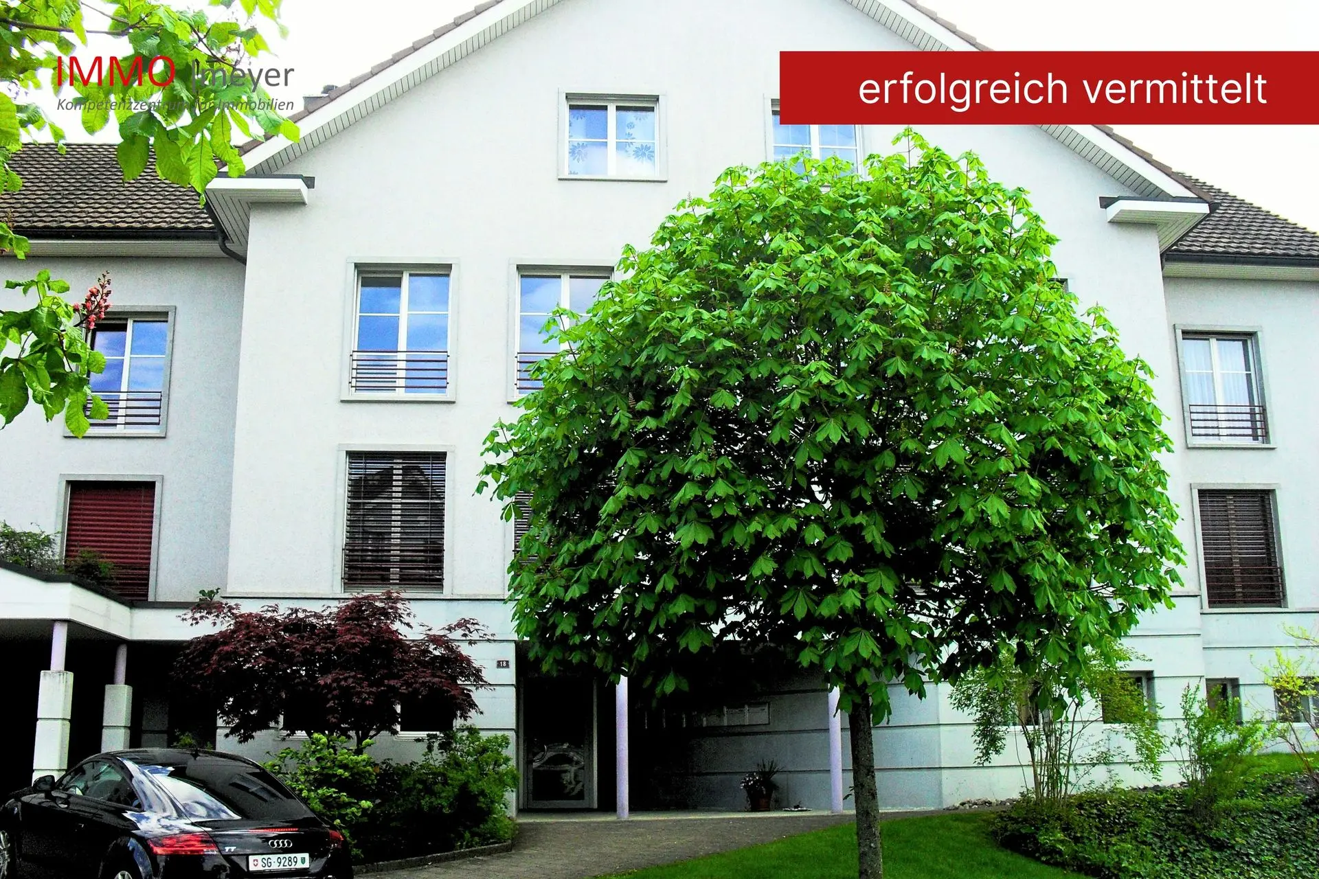 Mehrfamilienhaus mit grünem Vorgarten und Baum