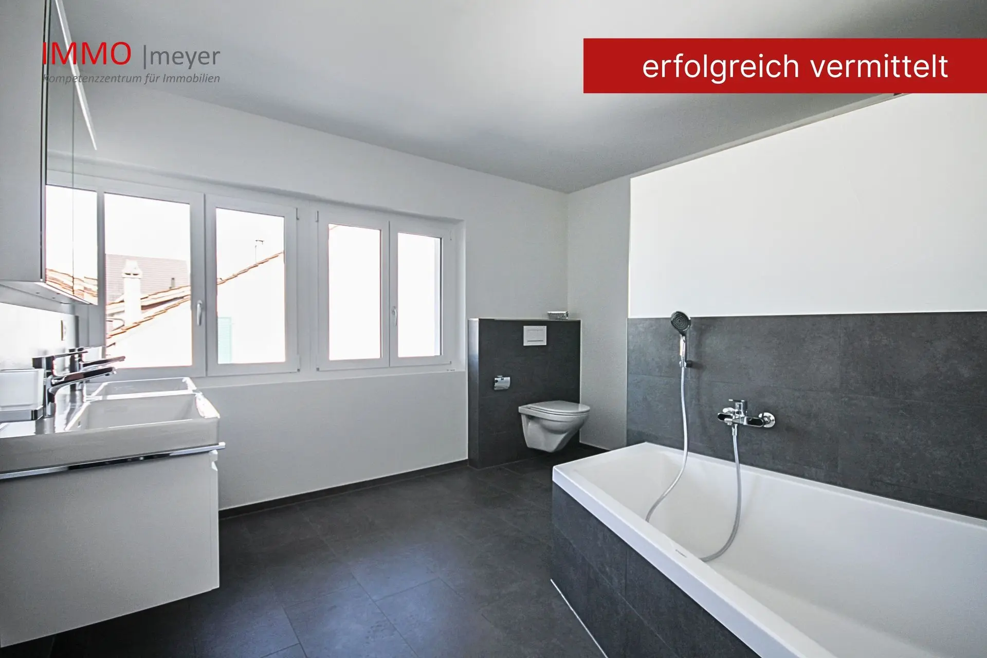 Badezimmer mit grauen Fliesen, Wanne und Toilette